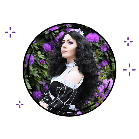 zdjęcie Arven Cosplay, czarnowłosa kobieta w czarnej ozdobnej sukni z profilu, w tle duży kwitnący krzew